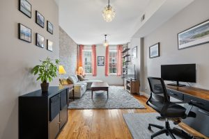 Current living room setup at 149 Webster Avenue #4 in Jersey City Heights, showing the flexible front room with hardwood floors, natural light, and an exposed brick accent wall.