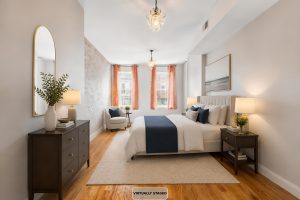 Virtually staged bedroom at 149 Webster Avenue #4 in Jersey City Heights, showing the flexible front room arranged with a bed and exposed brick accent wall.